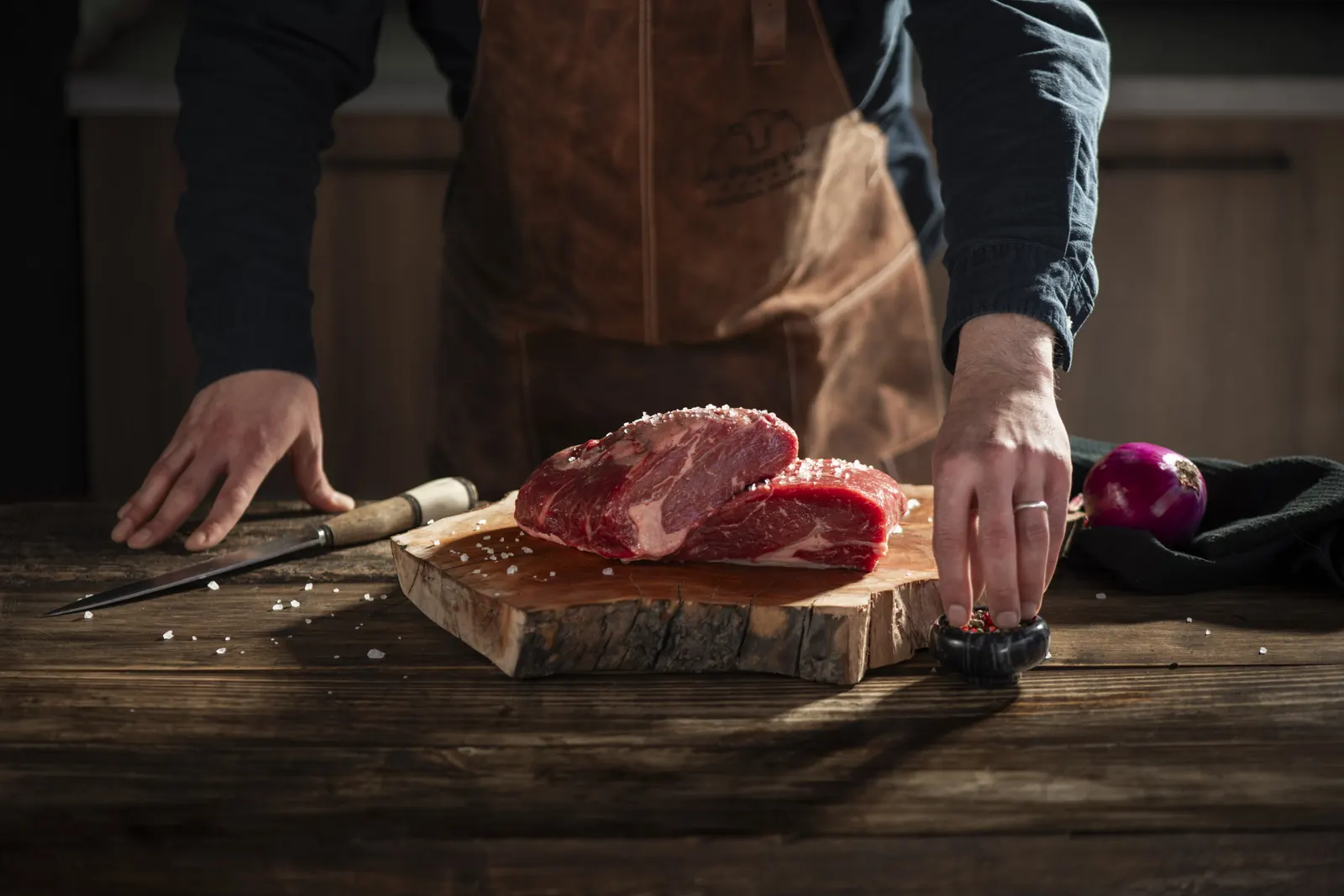 Carnicero A Punto con delantal de cuero salando un corte crudo sobre una tabla de madera